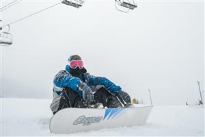 A snowboarder sitting with ski lifts in the background